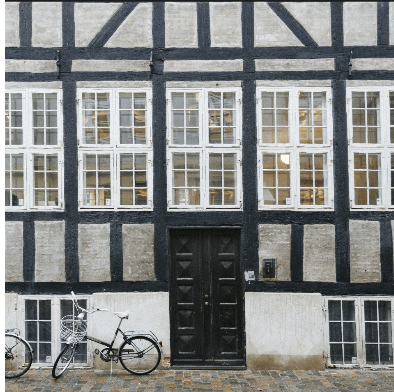 Fachwerkfassade mit sanierten weißen Holzfenstern und schwarzen Rahmen – Beispiel für Fenstersanierung und Rahmenaufbereitung im Altbau.