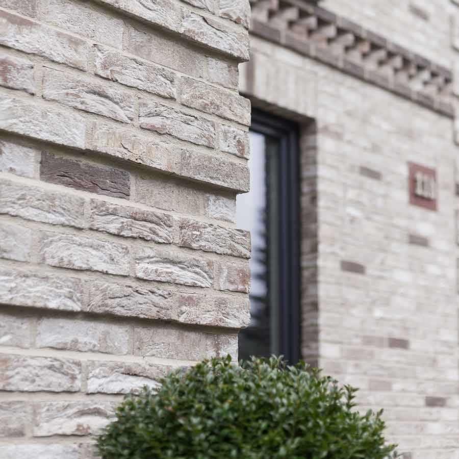 Nahaufnahme einer modernen Fassadengestaltung mit hellen, grau-beigen Klinkerriemchen und einem runden Zierstrauch Nahaufnahme einer modernen Fassadengestaltung mit hellen, grau-beigen Klinkerriemchen und einem runden Zierstrauch